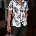 A man wearing a white short-sleeve button-up shirt with a black palm leaf pattern, paired with black shorts, holding a brown paper shopping bag.
