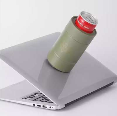 An olive green insulated can cooler with a debossed rose emblem, holding a red can, resting on the edge of a silver laptop against a clean white background.