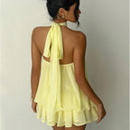 Woman wearing a yellow dress with a halter neck design on a plain background