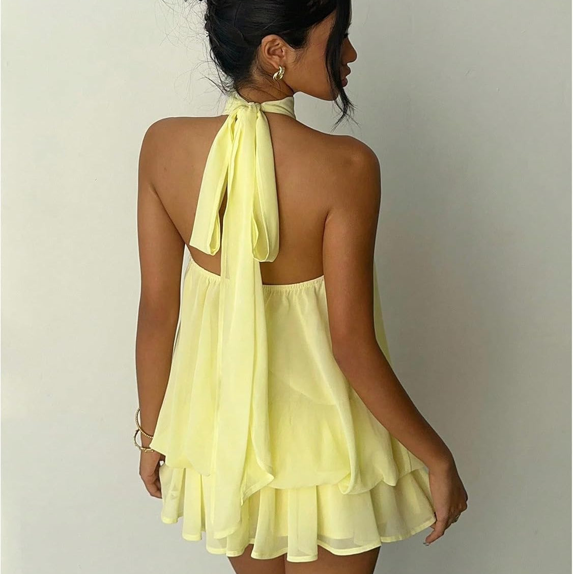 Woman wearing a yellow dress with a halter neck design on a plain background