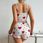 A woman shown from the back wearing a white ribbed two-piece romper with red heart prints and thin shoulder straps, standing indoors near a small table.