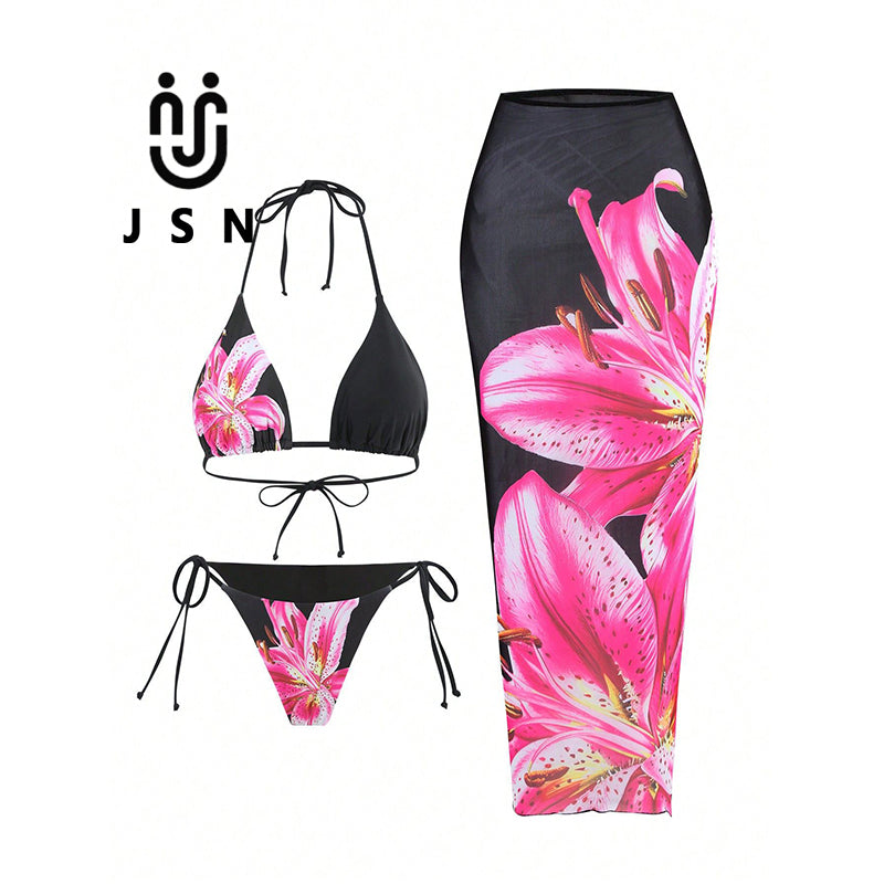 Three-piece women's bikini set on a white background, featuring a black halter top and matching side-tie bottoms with a large pink lily floral print, alongside a matching black midi skirt with the same floral pattern. The brand logo 'JSN' is visible in the top left.