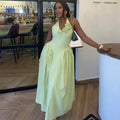 A woman wearing a pale yellow halter-neck maxi dress with a ruffled floral bodice, standing in a restaurant or bar interior next to a counter.