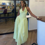 A woman wearing a pale yellow halter-neck maxi dress with a ruffled floral bodice, standing in a restaurant or bar interior next to a counter.