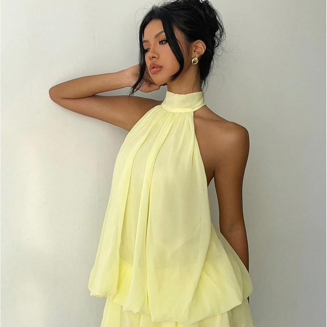 Woman wearing a light yellow halter neck dress against a plain background