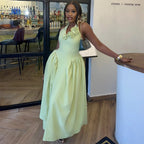 A woman wearing a sleeveless light mint green maxi dress with 3D floral embellishments on the bodice, standing in a restaurant or bar environment.