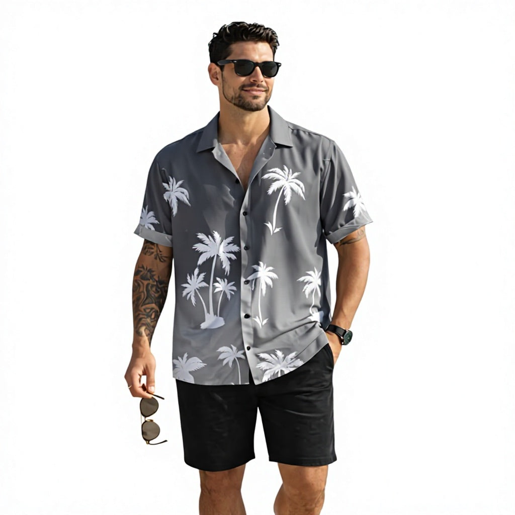 A man modeling a gray short-sleeve button-up shirt with a white palm tree pattern, paired with black shorts, against a plain white background.