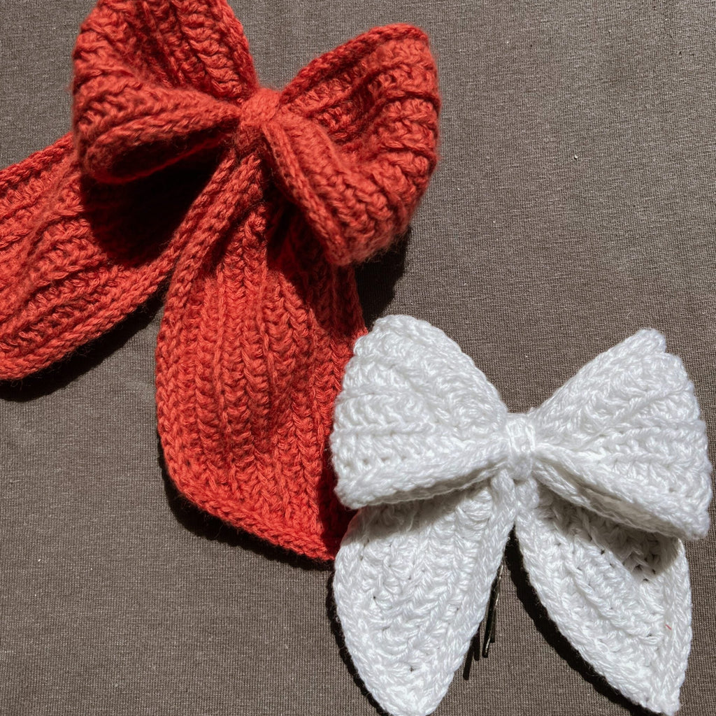 Two knitted bows, one red and one white, on a brown background.