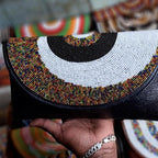 Hand holding a beaded clutch bag with colorful patterns in the background