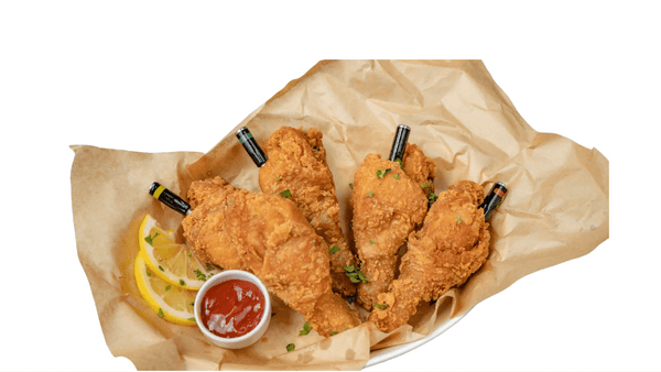 Breaded chicken wings on brown paper with lemon wedges and a dipping sauce. Mini Fried chicken thighs from Town Bakery