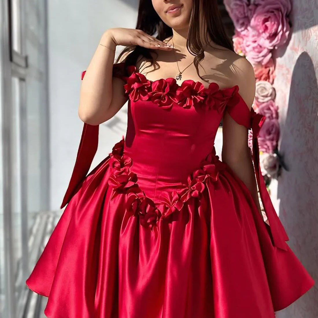 Red dress with floral details worn by a model against a decorative background.