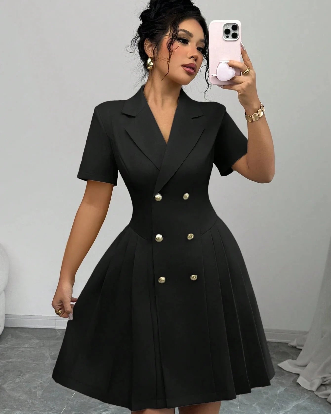 Woman wearing a black dress with buttons, taking a mirror selfie.