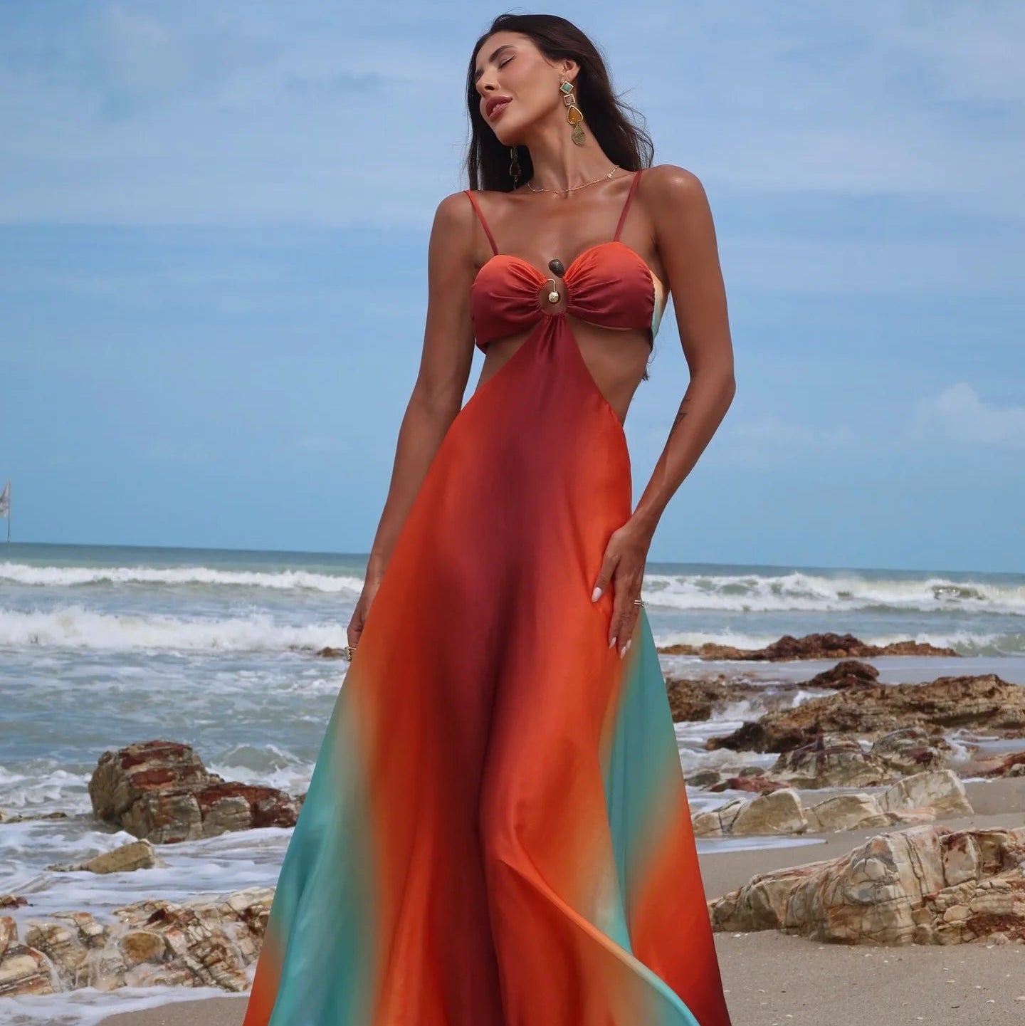 Woman in a colorful dress standing on a beach with ocean waves in the background