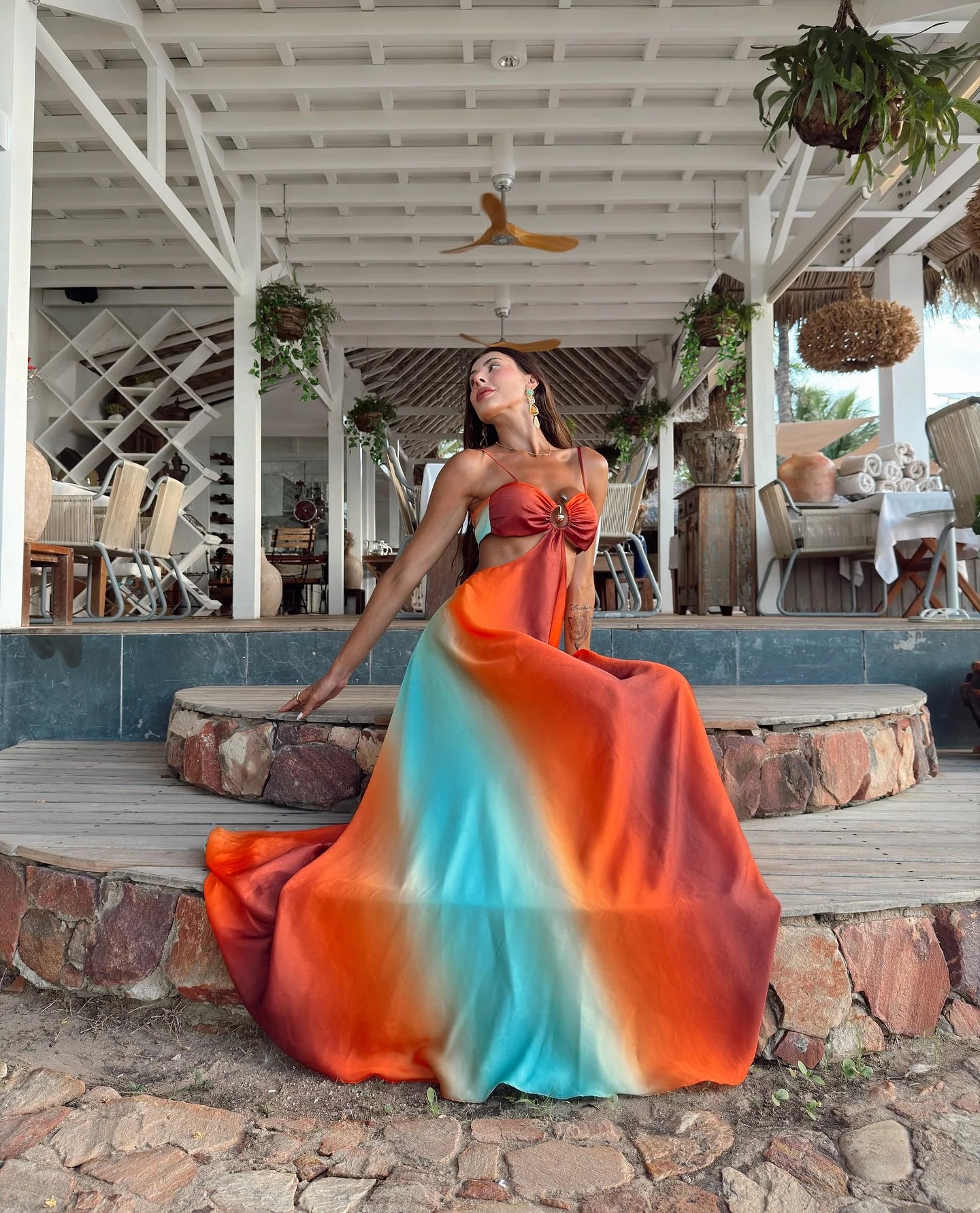 Woman in a colorful dress sitting on stone steps in a tropical setting.