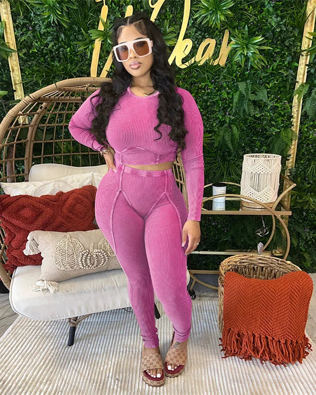 Woman in a pink outfit posing in a stylish outdoor setting with greenery and a decorative chair.