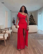 Woman in a red one-shoulder dress standing in a living room with a Christmas tree in the background.