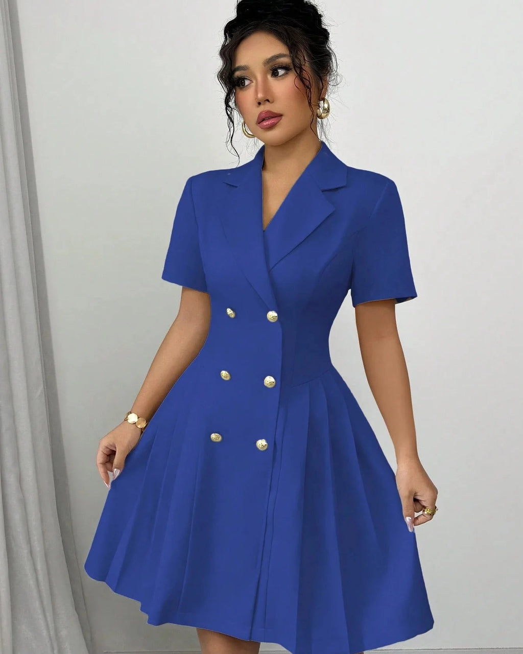 Woman wearing a blue dress with gold buttons against a gray background