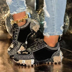 Black sneakers with rhinestone details worn with ripped jeans on a reflective surface.