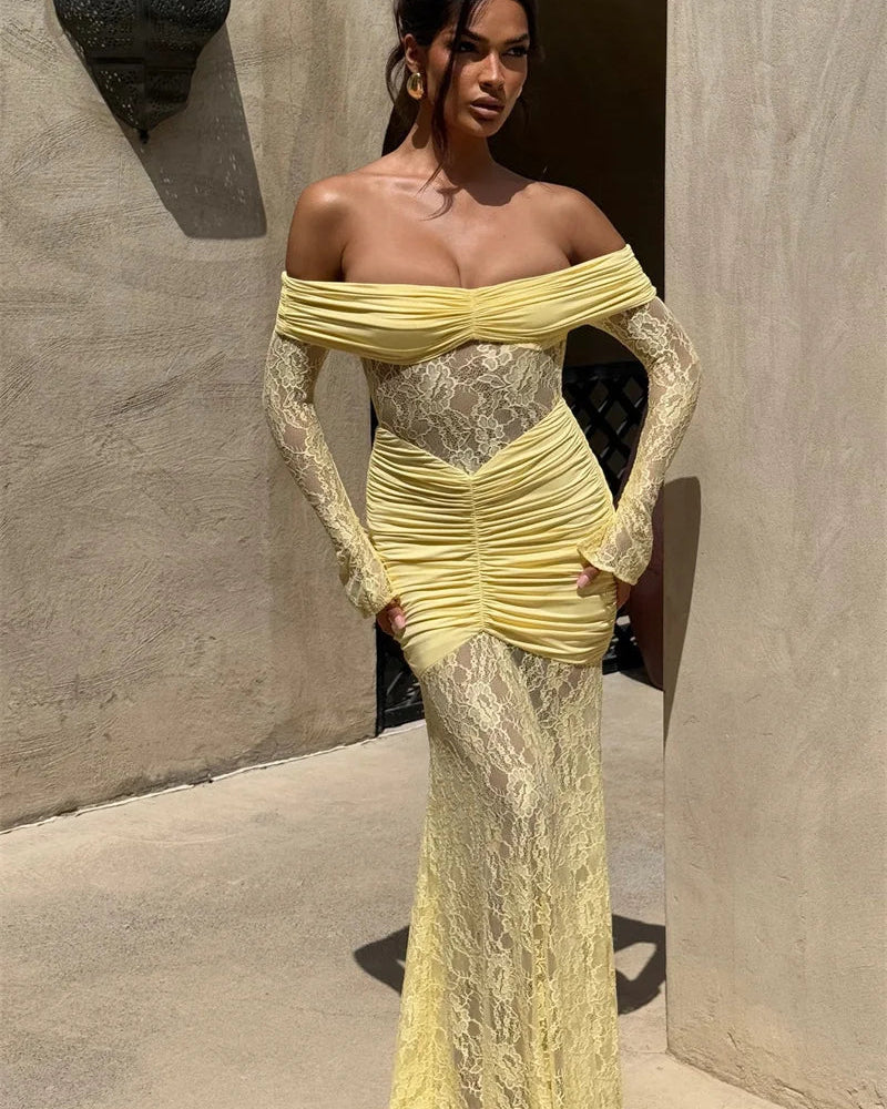 Woman in a yellow lace dress standing against a textured wall.