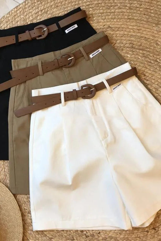 Three pairs of pants with belts on a textured surface, with a hat and sunglasses beside them.
