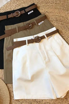 Three pairs of pants with belts on a textured surface, with a hat and sunglasses beside them.