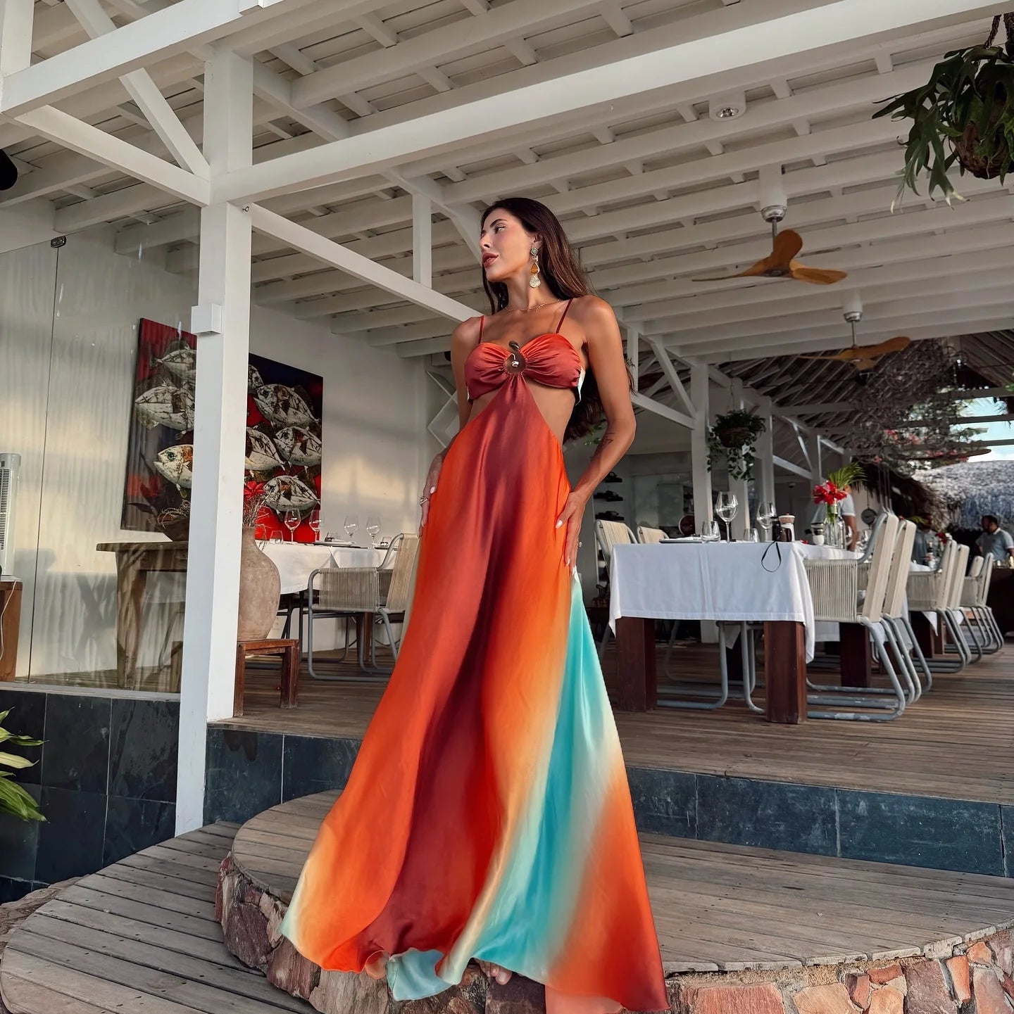 Woman in a colorful dress standing on a wooden platform with a restaurant interior in the background.