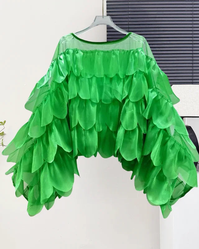Green ruffled top on a hanger against a white wall.