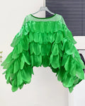 Green ruffled top on a hanger against a white wall.