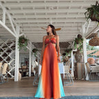 Woman in a colorful dress standing in a tropical setting with wooden deck and plants.