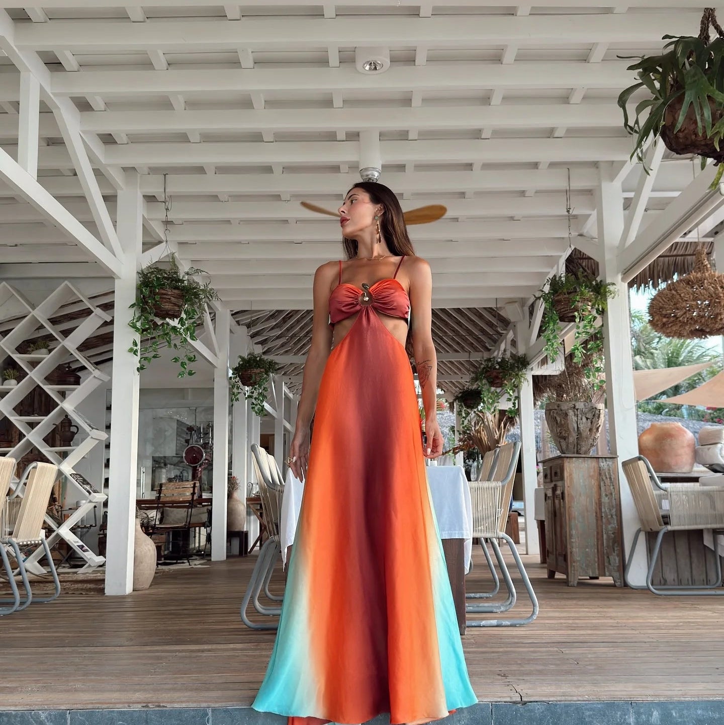 Woman in a colorful dress standing in a tropical setting with wooden deck and plants.