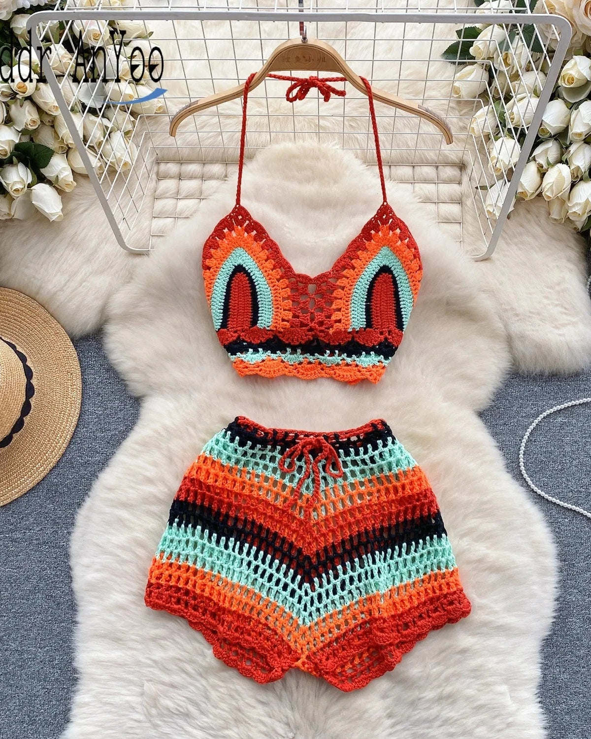 Colorful crochet bikini set on a hanger with flowers and a hat in the background