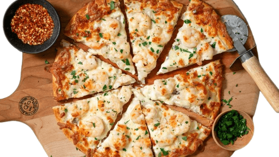 Pizza sliced on a wooden board with a side of sauce and greens. Shrimp pizza from Town Bakery 2