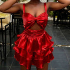 Woman wearing a red satin dress with a bow detail in an outdoor setting.