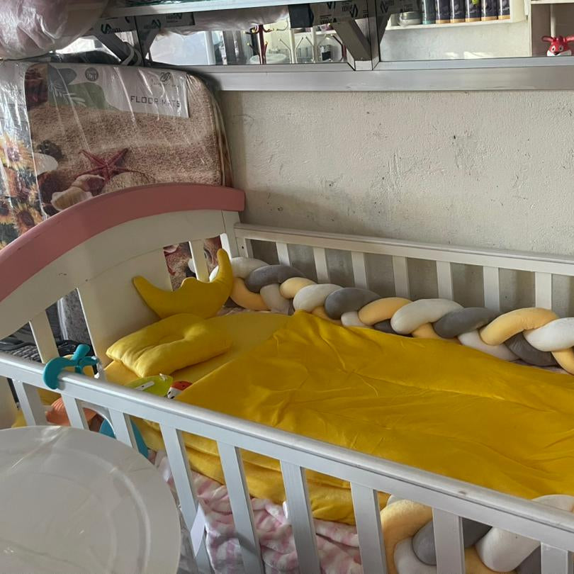 White crib with yellow blanket and colorful toys in a room with a mirror on the wall.