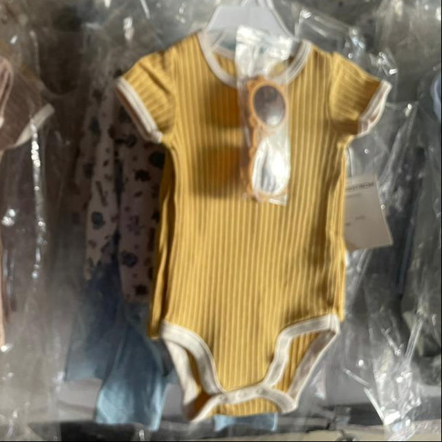 Two baby rompers on hangers with tags, one brown and one yellow, in a clear plastic bag.