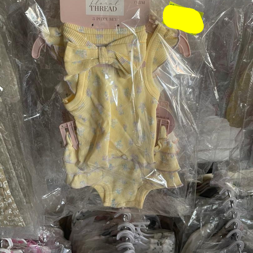 Yellow baby outfit with matching headband on a hanger, wrapped in clear plastic with a price tag.