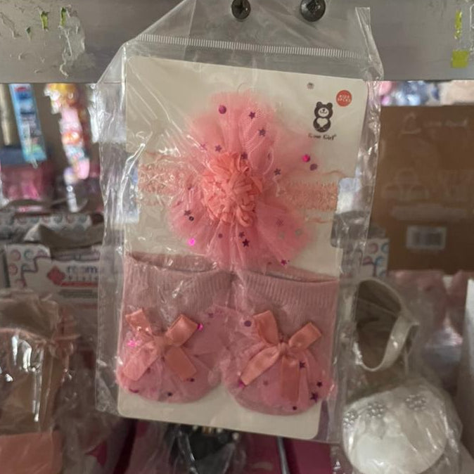 Pink baby shoes with decorative elements in clear packaging on a store shelf.