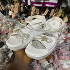 White sandals with decorative straps on a background of various shoes