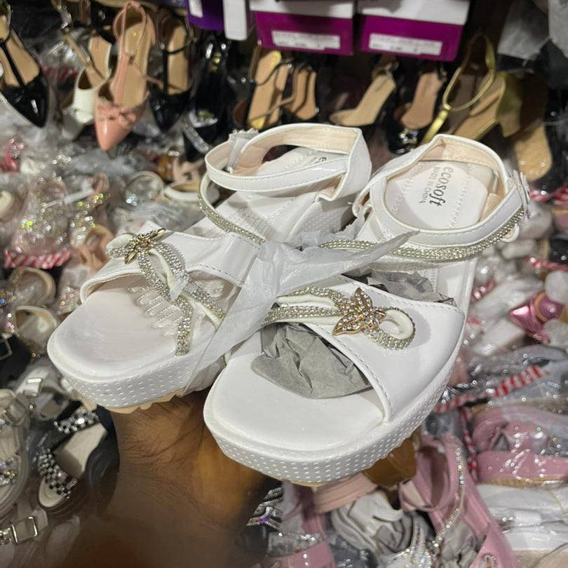 White sandals with decorative straps on a background of various shoes