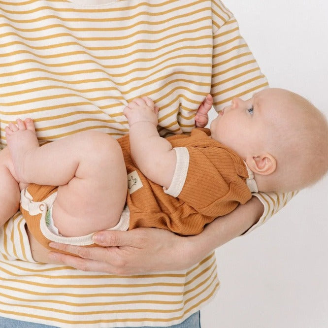Person holding a baby wearing a striped shirt and orange outfit against a plain background