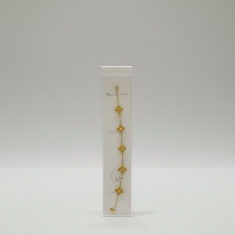 Gold bracelet on a clear plastic card with brand name, on a reflective surface.
