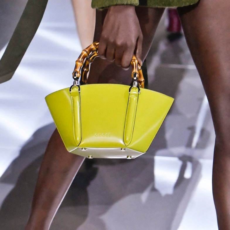 Yellow handbag with gold handles held by a person on a reflective surface