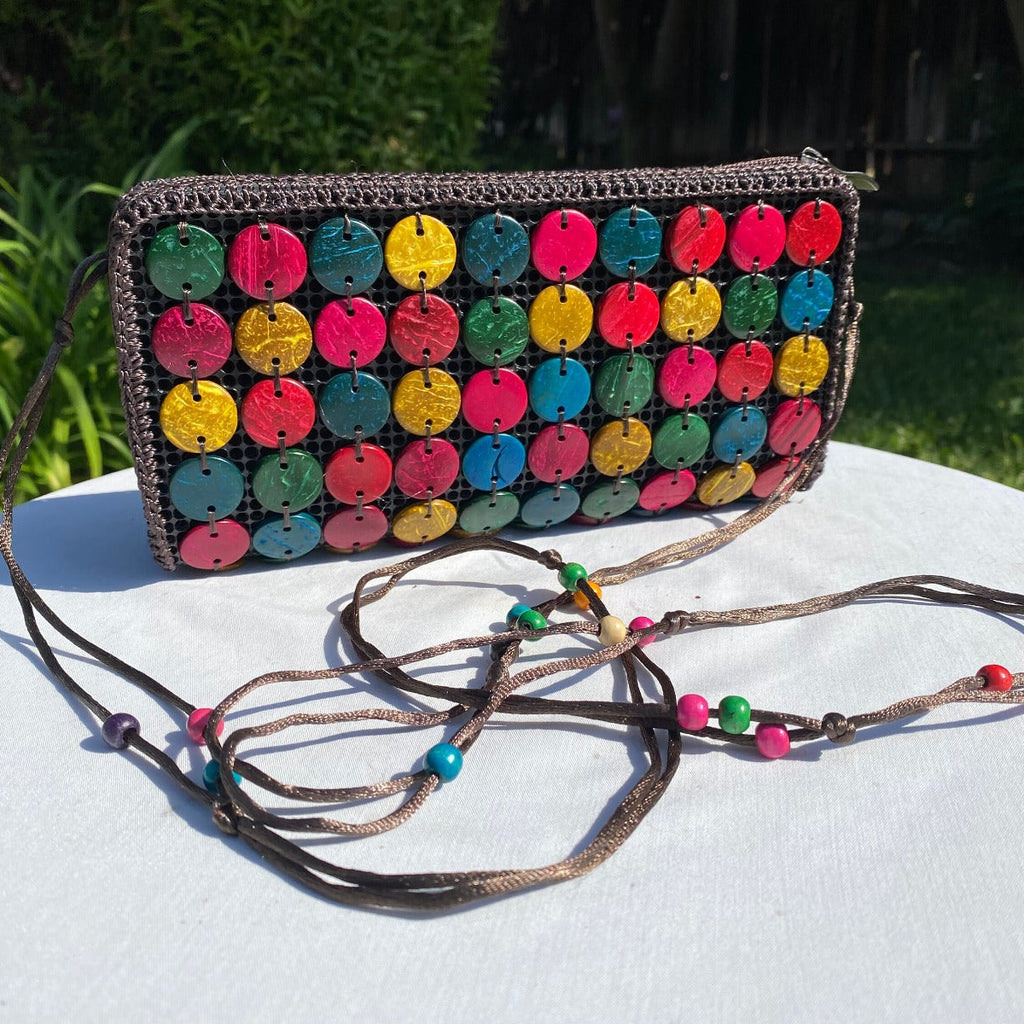 Colorful polka dot clutch bag with a textured strap on a white surface outdoors.