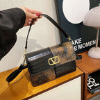 Handbag with floral and crocodile pattern held by a hand on a wooden surface.