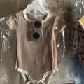 Two baby rompers on hangers with tags, one brown and one yellow, in a clear plastic bag.