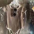 Two baby rompers on hangers with tags, one brown and one yellow, in a clear plastic bag.
