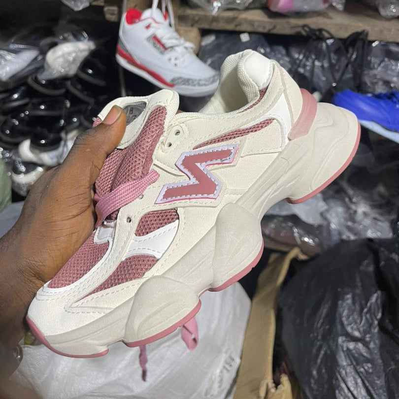 Beige and pink sneakers held by a hand in a store setting with various items in the background.