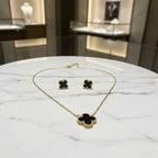 Gold necklace with black clover pendants on a reflective surface