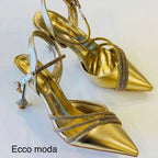 Gold high-heeled shoes with strappy design on a light background, featuring the brand 'Ecco moda'.