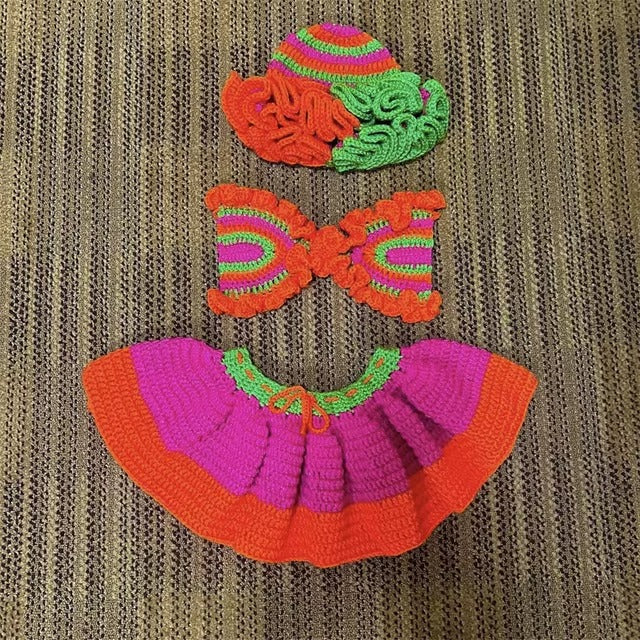 Colorful crochet set including a top, skirt, and headband on a textured fabric background.
